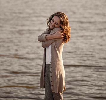 imagem de mulher se abraçando sorrindo em frente ao mar