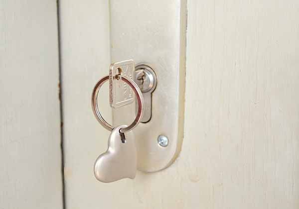 detalhe de porta na cor bege com fechadura e chave com chaveiro em formato coração