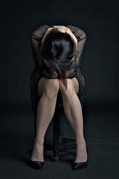 mulher sentada em uma cadeira com as mãos sobre a cabeça abaixada
